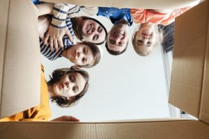 Szczęśliwa rodzina - zdjęcie robione z dołu, z wnętrza kartonowego pudła, nad którym pochylają się uśmiechnięci rodzice i dzieci