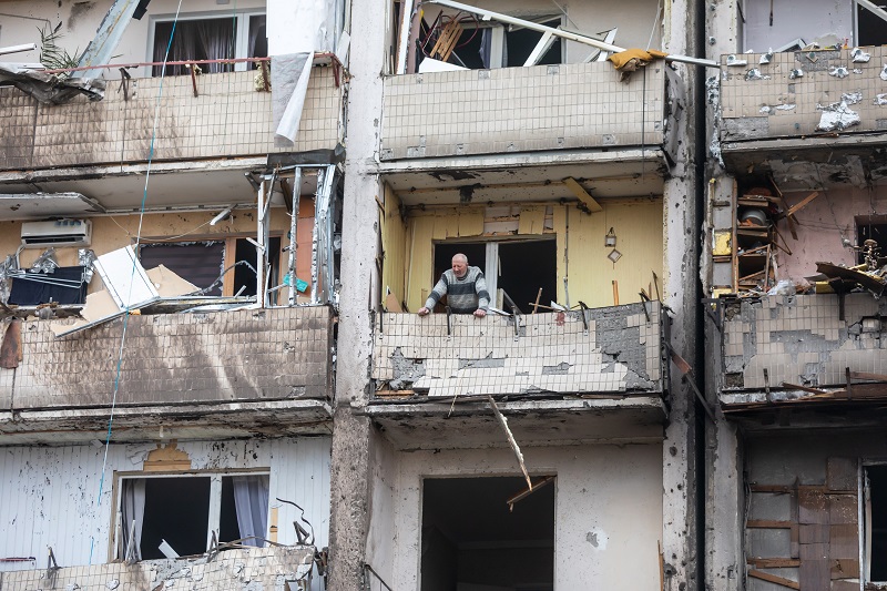 Mężczyzna stojący na balkonie bloku zniszczonego ostrzałem